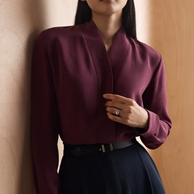 A woman wearing a long sleeve maroon silk top with black trouser pants and black belt