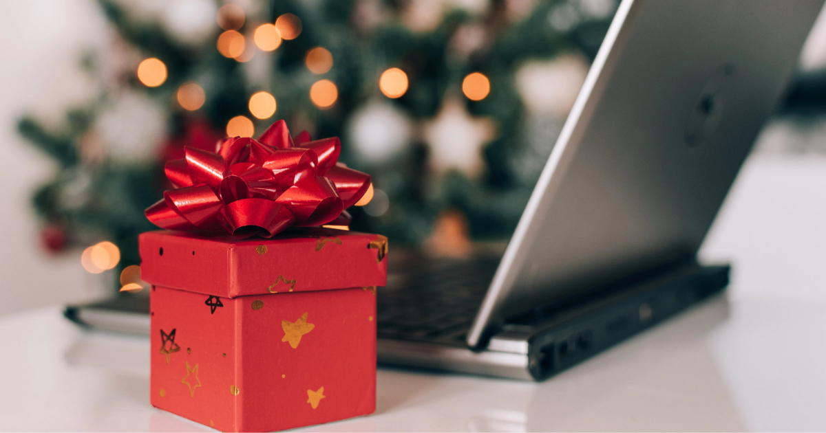 red present box sits in front of a laptop; a Christmas tree is in the background
