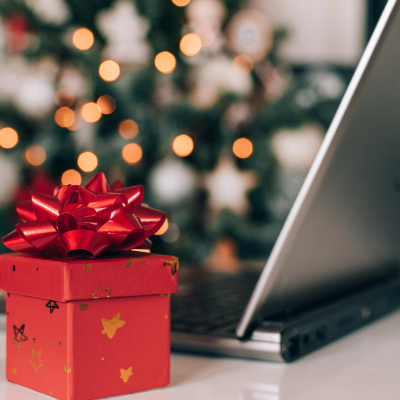 red present box sits in front of a laptop; a Christmas tree is in the background