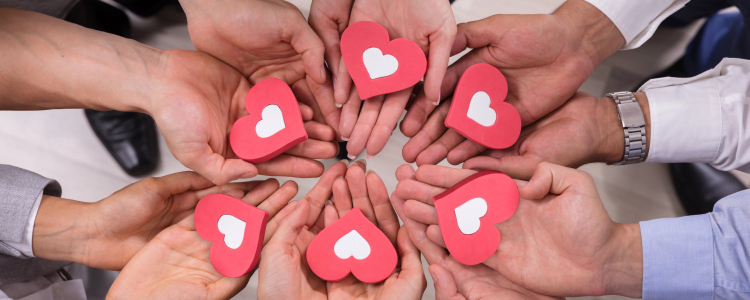 Several people's hands coming together in a circle, with each person holding a red heart