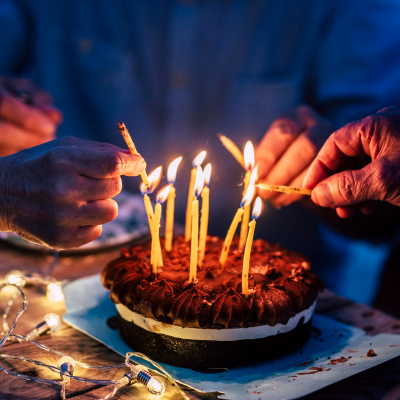 group of people with old and young-looking hands light candles on a chocolate cake