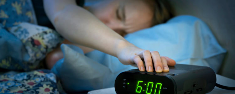 sleepy woman reaches out of bed to slam her hand down on her alarm clock; she's wishing she had a better one for 2026!