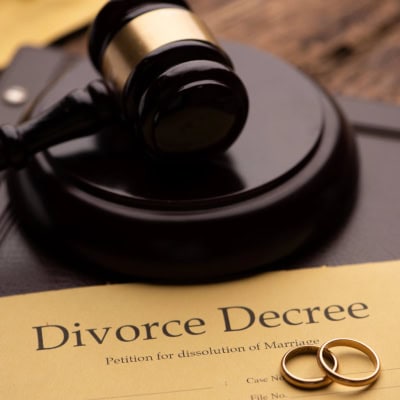 a paper reading DIVORCE DECREE lays on a table, with two wedding rings laying on top of it; just above the paper is a gavel