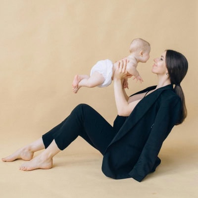 young stylish professional woman holds a baby; she has a blazer resting on her shoulders but is not wearing it