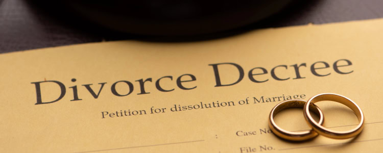 a paper reading DIVORCE DECREE lays on a table, with two wedding rings laying on top of it; just above the paper is a gavel