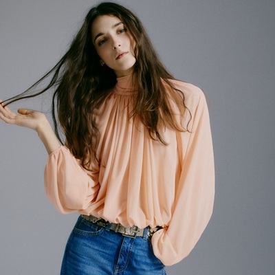 A woman wearing blue jeans, belt, and peach blouse
