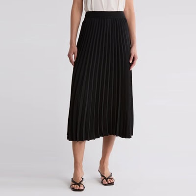 A woman (only the bottom half of her body is shown) wearing a white top, black pleated skirt, and black sandals