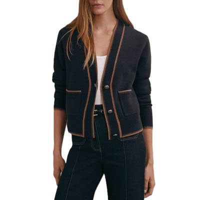 A woman wearing black pants, black belt, white top, and navy pocket cardigan with brown trim