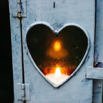 a candle burns behind a heart-shaped cutout