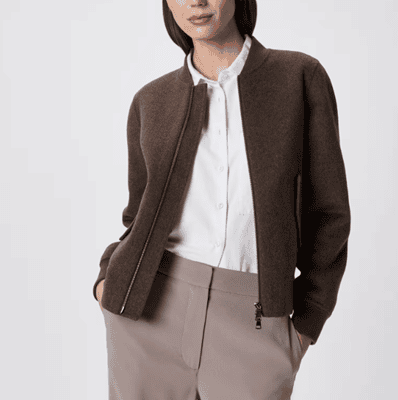 woman wears brown merino bomber jacket, crisp white blouse, and tan wide-legged pants