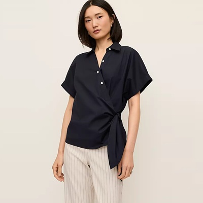 A woman wearing a black tie-waist top and striped ivory pants