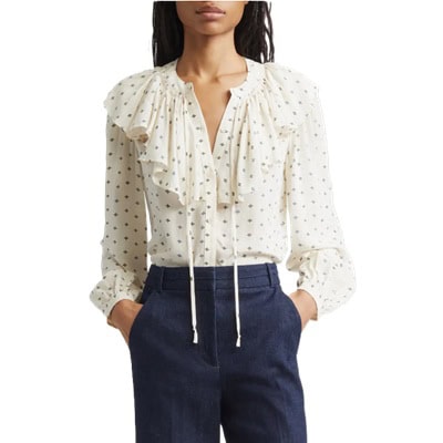 A woman wearing a ruffle-front ivory printed top and tailored denim pants