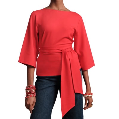 A woman wearing a red wrap top, dark blue jeans, and multiple red bracelets