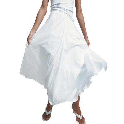 A woman (lower half of body shown) wearing a white top, white skirt, and white sandals