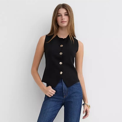 A woman wearing blue jeans and a black vest with metal buttons