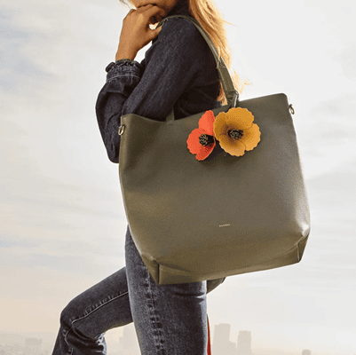 woman carries large olive green tote with orange leather poppy-shaped "charms" dangling from the handles