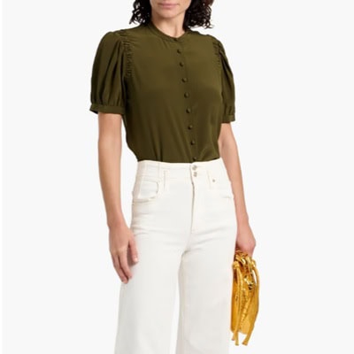 A woman wearing a short-sleeve olive top with off-white pants, and carrying a gold handbag in one hand