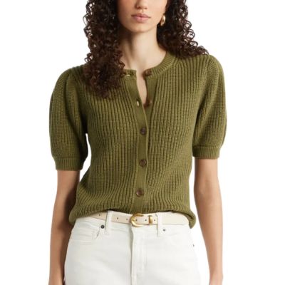 A woman wearing an olive green cardigan, white pants, and a cream-colored belt