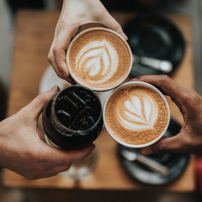 friends toast with lattes and another dark drink that is possibly soda or cold brew