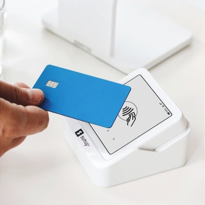 person holds blue credit card at a payment station (tap to pay)
