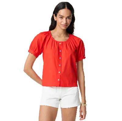 A woman wearing a bright orange button-front shirt and white shorts