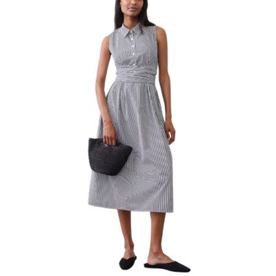 A woman wearing a sleeveless white-and-navy striped shirtdress and black flats. She is carrying a black woven bag.