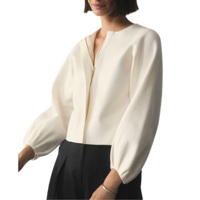 A woman wearing an ivory collarless blazer and black pants