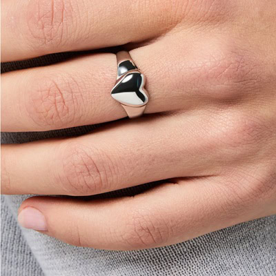 A woman's four fingers in front of her gray clothes; she is wearing a silver tone heart ring