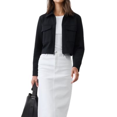 A woman wearing a black blazer, white top, white skirt, and carrying a black handbag