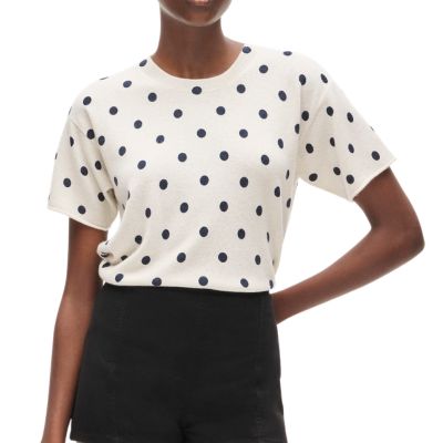 A woman wearing and ivory-and-navy polka dot top and black shorts
