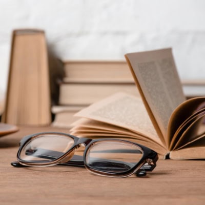 beige books stacked on a table, with eyeglasses and a coffee cup also
