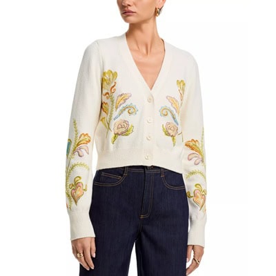 A woman wearing dark blue jeans and an ivory cardigan with floral embellishments 