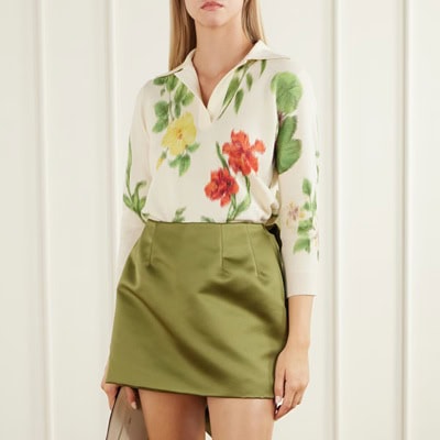 A woman wearing a floral top (white, red, green, and yellow) and olive green skirt