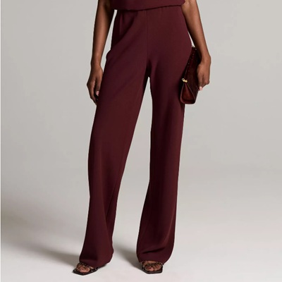 A woman (bottom half of body shown) wearing burgundy pants, a matching top, and sandals