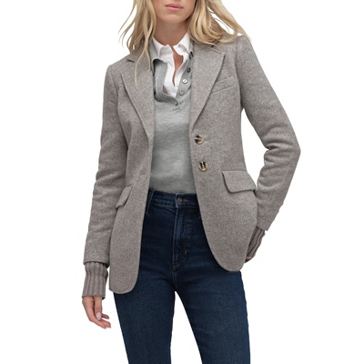 A woman wearing a gray polo shirt, gray blazer, and dark blue jeans