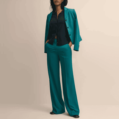 polished Black woman wears teal green suit; the suit jacket is just laid over her shoulders