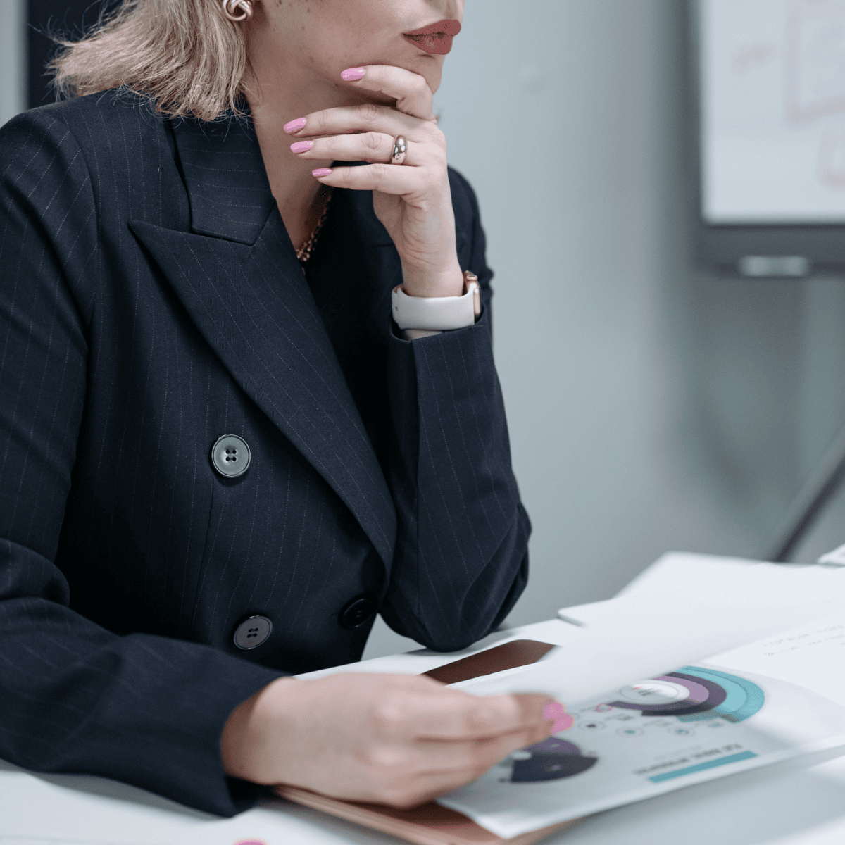professional young woman in blazer has contemplative expression on her face; she is holding a piece of paper