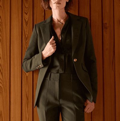 woman wears olive green suit; she has her hand on the lapel
