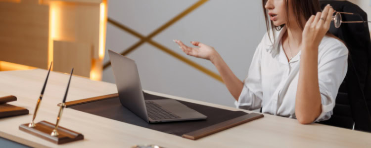 Woman sighs in exasperation at something on her laptop; she has taken off her eyeglasses and holds one hand out in a WTF gesture