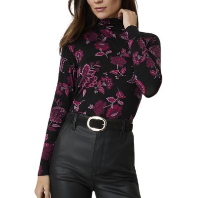 A woman wearing black pants, a black belt, and pink, purple, and black floral top