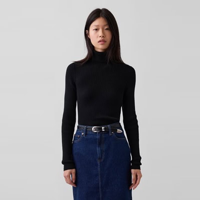 A woman wearing a long blue denim skirt, black belt, and black turtleneck