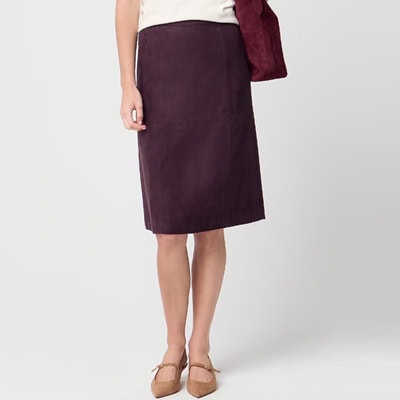 A woman wearing a white top, tan kitten heels, and a purple-y brown midi skirt. She is carrying a brown handbag