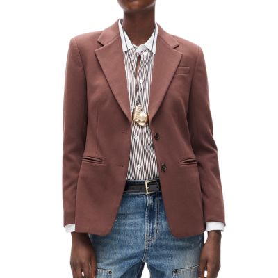 a woman wearing a brown blazer, pinstriped shirt, two necklaces, black belt, an blue jeans