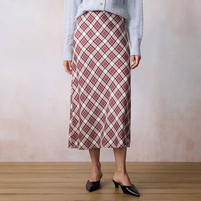 A woman wearing a red plaid midi skirt, black mules, and a light blue sweater