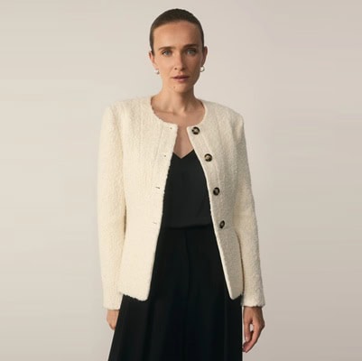 A woman wearing an ivory boucle jacket, black top, and black pants