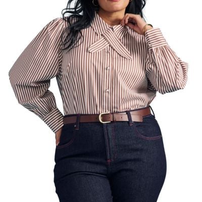 A woman wearing a brown-and-white pinstripe blouse, dark blue jeans, and a brown belt