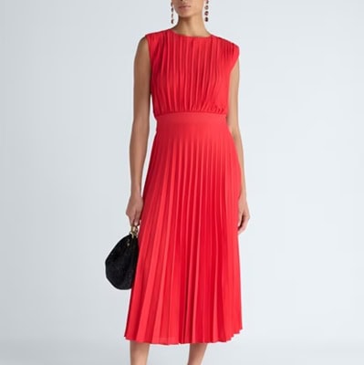 A woman wearing an orange midi dress and carrying a black bag