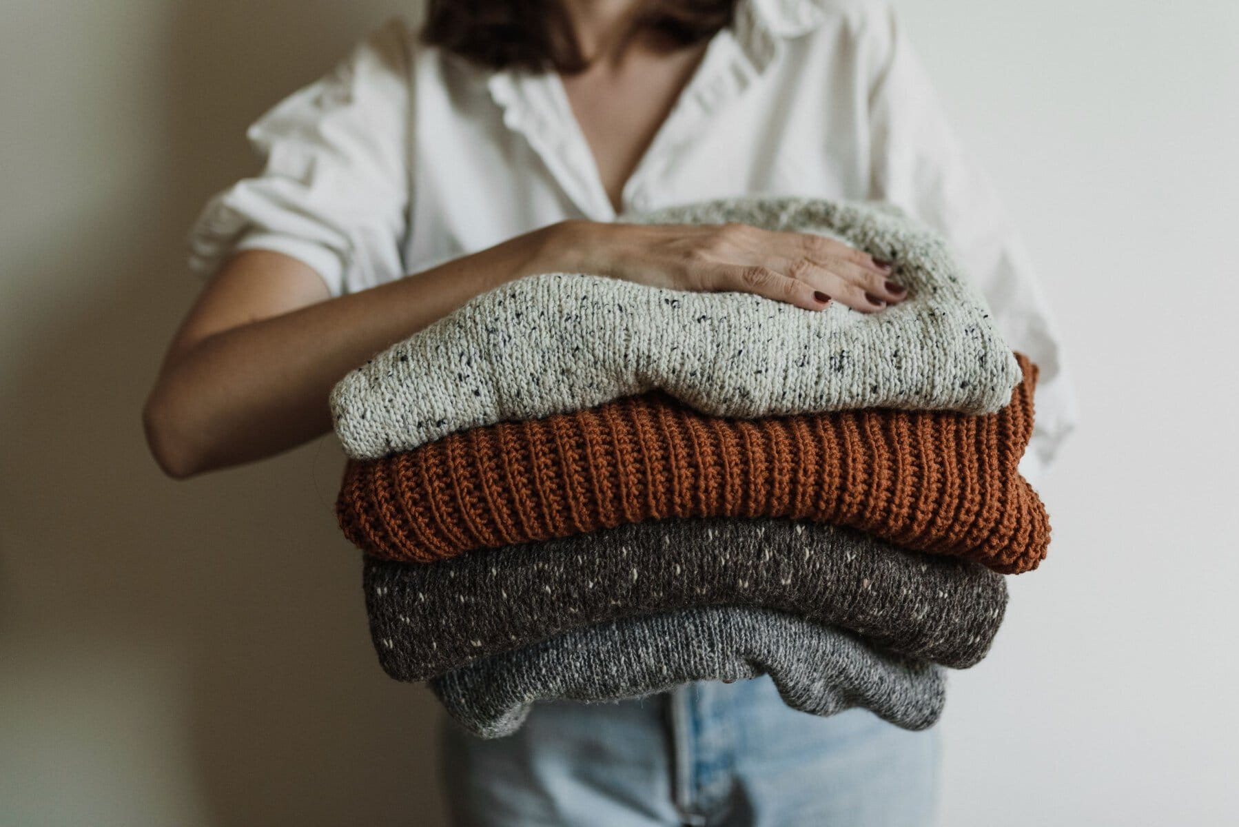 A woman holding a stack of cozy, warm knit sweaters, perfect for winter.