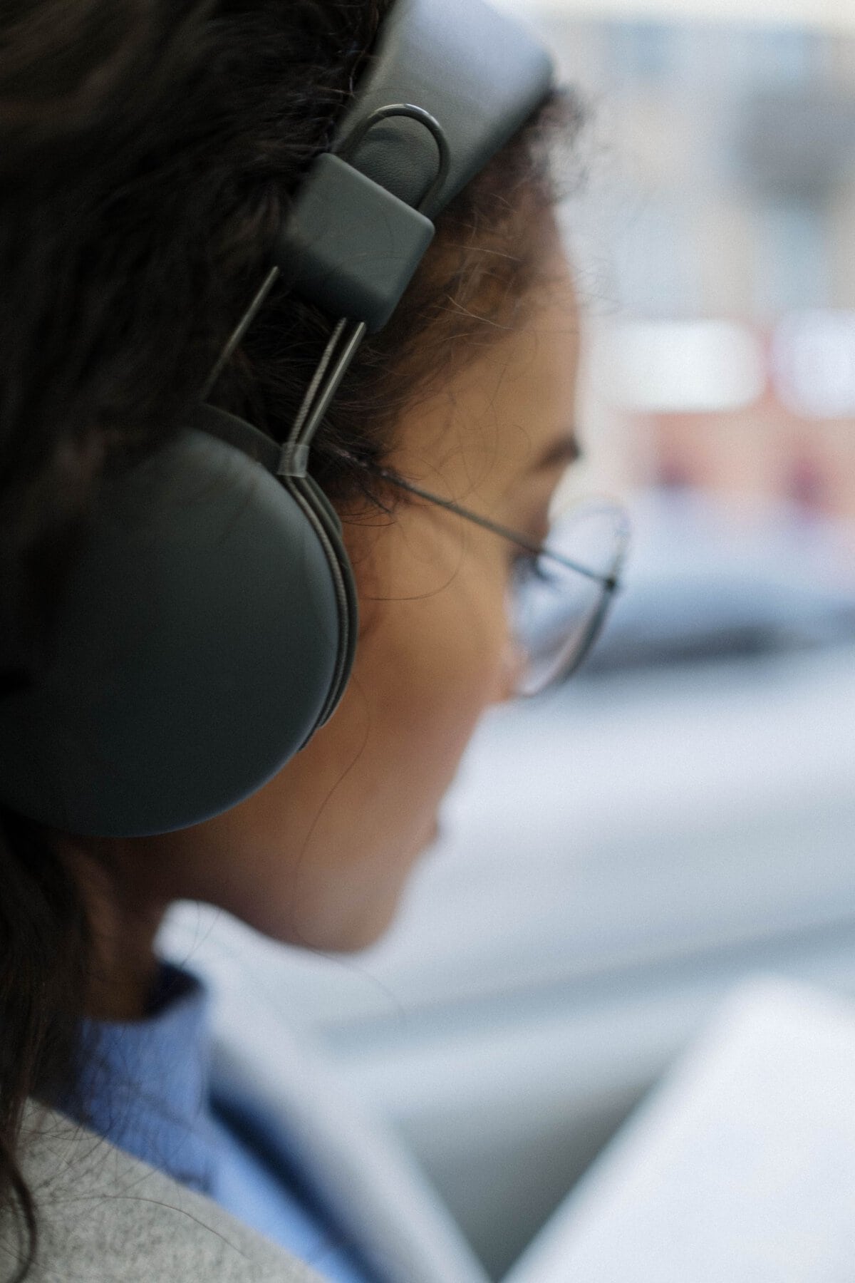 A woman wearing black headphones and glasses is focused on a task.