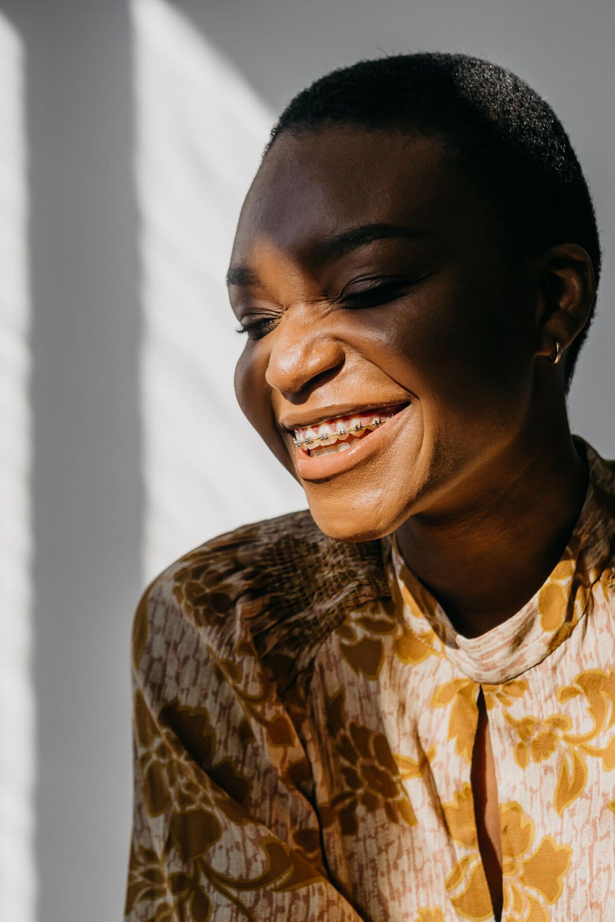 Bright portrait of a black woman with a shaved head, wearing floral print, showcasing beauty with braces and a glowing smile.